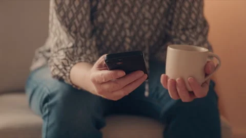 Middle-aged woman using mobile phone while holding coffee cup at home, rela.. Stock Footage 344860241