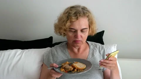 Middle aged woman using smart phone eating breakfast in bed at home, female.. Stock Footage 230255659