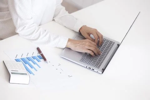 Middle-aged woman's hands typing on a laptop while analyzing statistics and.. Stock Photos