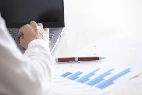 Middle-aged woman's hands typing on a laptop while analyzing statistics and.. Stock Photos