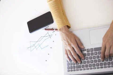 Middle-aged woman's hands typing on a laptop while analyzing statistics and.. Foto stock