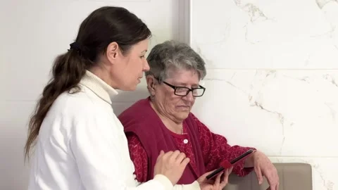 A middle-aged women explains the settings on a cell phone to an grandmother Stock Footage 262550880