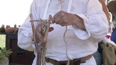 Middle Ages tools. A man wearing medieval clothes, braiding a hemp rope. Video stock 76141507