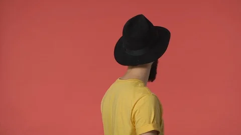 Middle-eastern bearded man in black hat, yellow t-shirt standing backwards turn Stock Footage 115777812