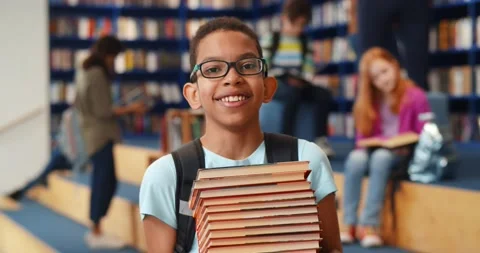 Middle eastern boy holding stack of books against multi colored bookshelf in Stock Footage 151411217