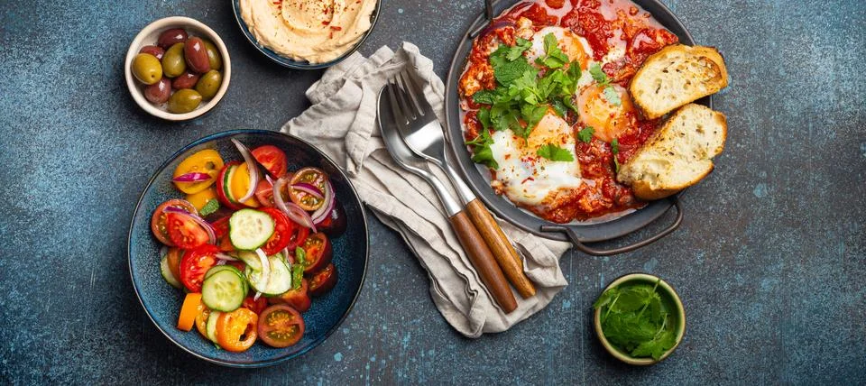 Middle Eastern breakfast or brunch with Shakshouka in pan, toasts, vegetables Foto stock