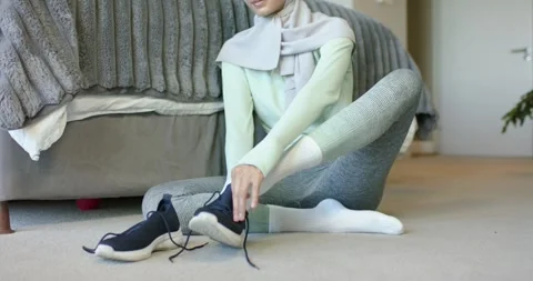 Middle Eastern female in hijab sitting in bedroom by bed, putting on navy Stock Footage 340011503