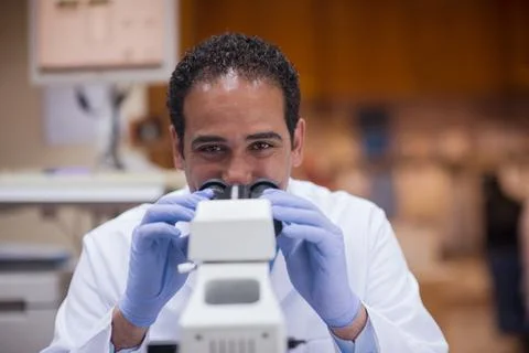 Middle Eastern lab technician looking through microscope in clinical blood 스톡 사진