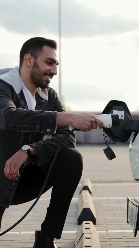 Middle Eastern male plugging a charger into the socket of an electric car Stock Footage 275011964