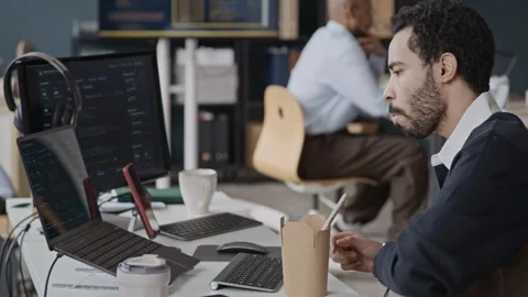 Middle Eastern Man Eating Lunch at Desk and Coding on Laptop in IT Office Stock Footage 337474031