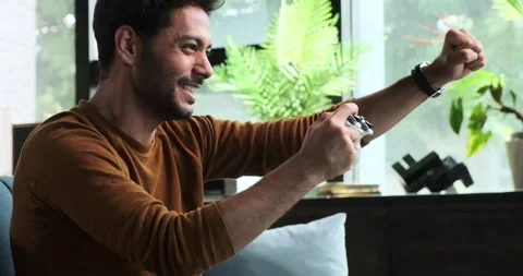Middle Eastern Man with Gamepad Victorious in Video Game on Sofa Stock Footage 254442184