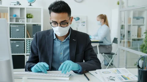Middle Eastern man wearing mask and gloves working with computer in office room Stock Footage
