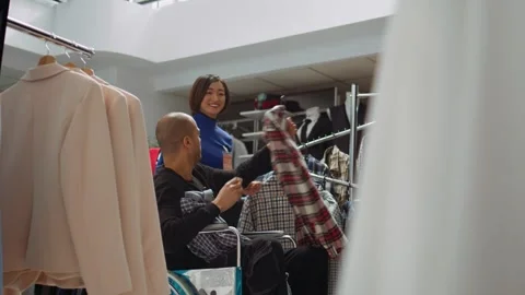 Middle eastern man in wheelchair choosing clothes to try on in the fitting room Stock Footage 319517543