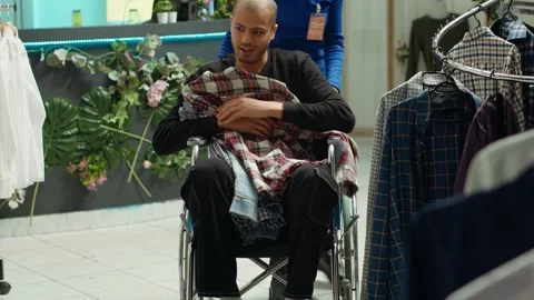 Middle eastern man in wheelchair choosing clothes to try on in the fitting room Stock Footage 319532733