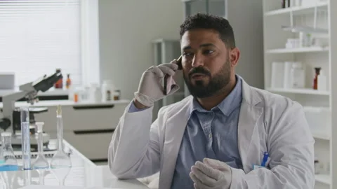 Middle Eastern Scientist Speaking on Mobile Phone at Desk in Laboratory Stock Footage 312474324