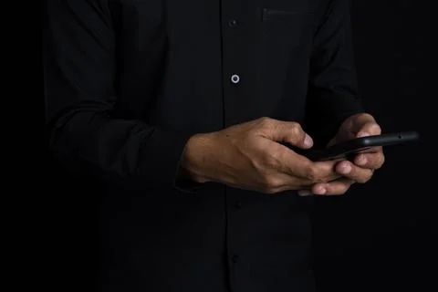 Middle part of businessman using smart phone while standing with black back.. Photos