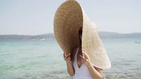 Middle shot of lady in summer hat and white swimsuit, standing by the water Stock Footage 147962901