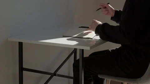 Middle shot: Unrecognizable Man Sits Down At The Table and starts writing Video stock 229896554