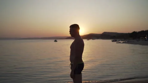 Middle shot of young man standing near the sea watching the sunset and breathing Stock Footage 147407847