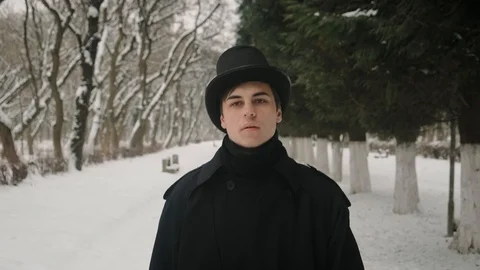 Middle view shot: A man in a black cloak and hat walks in the park alley. 60fps Stockbeeldmateriaal 102191856