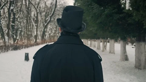Middle view shot: A man in a black cloak and hat walks in the park alley. 60fps Stockbeeldmateriaal 102202186