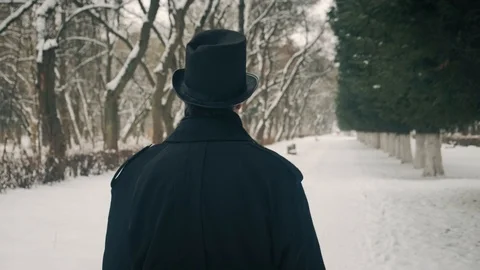 Middle view shot: A man in a black cloak and hat walks in the park alley. 60fps Stockbeeldmateriaal 102202320