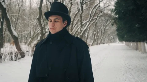 Middle view shot: A man in a black cloak and hat walks in the park alley. 60fps Stockbeeldmateriaal 102203404
