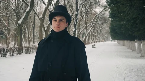 Middle view shot: A man in a black cloak and hat walks in the park alley. 60fps Stockbeeldmateriaal 102203453