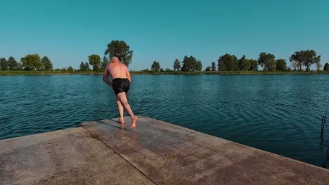 Middle years man run on dock or pier and jump into refreshing cool water of lake Stock Footage 305997467