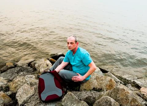 Midle aged man sitting on the shore of the lake. Solitude mature man sitting on Stock-Fotos
