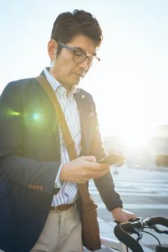 Midsection of asian businessman using smartphone holding bike in city street 写真素材
