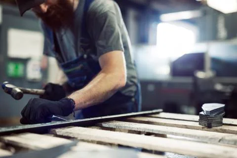 Midsection of blue collar worker using hammer and chisel in steel factory Fotos de archivo