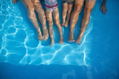 Midsection of family with small children sitting in swimming pool outdoors. Stock Photos