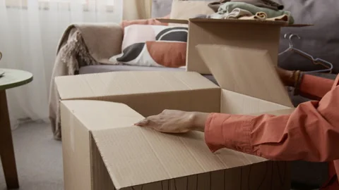 Midsection of Girl Packing Clothing Items for Donation and Sealing Box with Tape Stock Footage 335162829