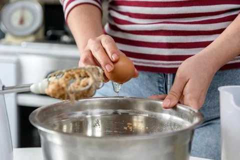 Midsection image of woman cracking egg over mixing bowl. Person cooking and b Stock Photos