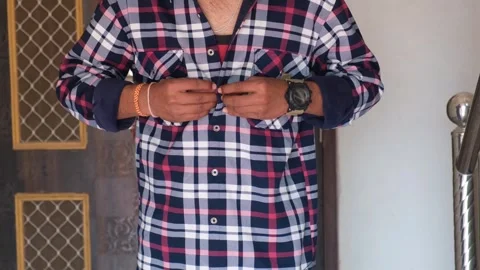 Midsection of a man in a blue and red plaid shirt buttoning his sleeve Stock Footage 329922083