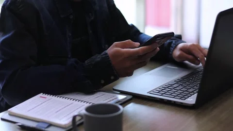 Midsection of man texting on smartphone and using laptop at desk Stock Footage 273059455