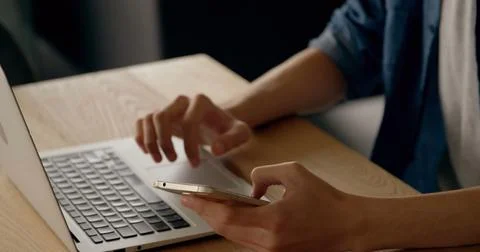 Midsection of man texting on smartphone and using laptop at desk Stock Photos
