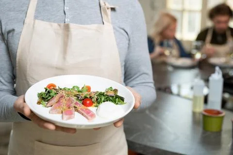 Midsection of mature man in pullover and apron holding plate with selfmade Stock Photos