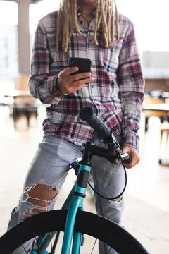 Midsection of mixed race man with dreadlocks sitting on bicycle in street using Stock Photos