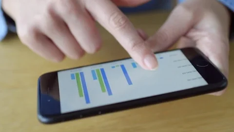 Midsection pan of woman scrolling through graphs on smart phone Stock Footage 70179326