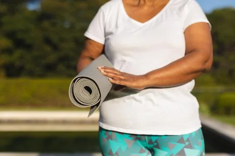 Midsection of senior african american woman with yoga mat by outdoor pool in Stock Photos