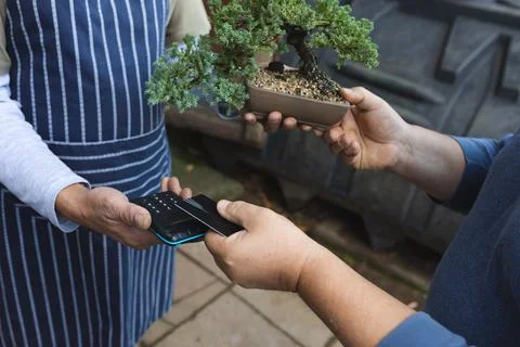 Midsection of two diverse men using contactless payments at garden centre Stock Photos