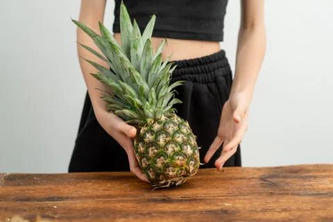 Midsection view of individual holding a pineapple on wood surface. Stock Photos