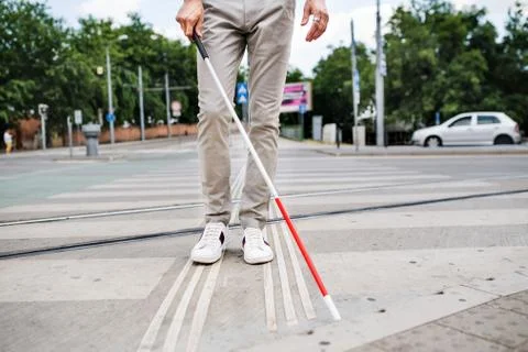 Midsection of young blind man with white cane walking across the street in city. Stock Photos
