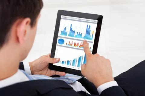 Midsection of young businessman comparing graphs on digital tablet in office Stock Photos