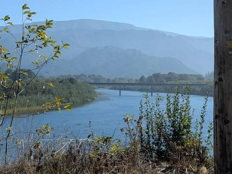 The mighty Klamath River flows beneath a vast bridge, surrounded by forests Photos