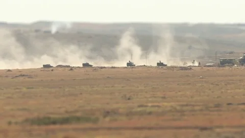 A military convoy of tanks and armored vehicles rides through the desert raising Stock Footage
