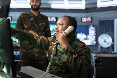 Military dispatcher pointing at screen while speaking on landline phone Stock Photos