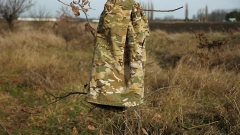 A military jacket is hanging on a tree, and the military is stationed in a field Stock Footage 317000521